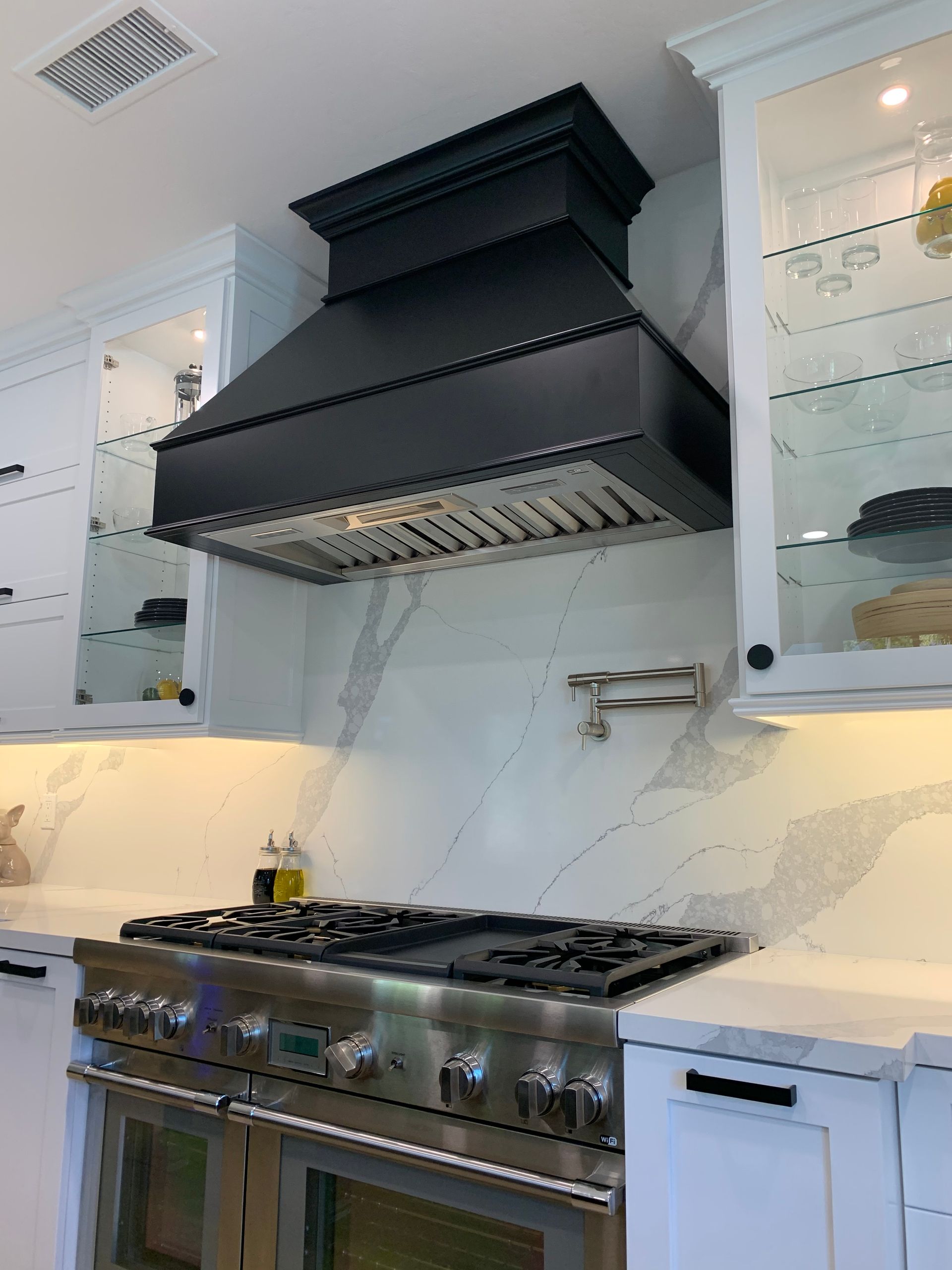 Modern kitchen with stainless steel gas range, black range hood, and white cabinets