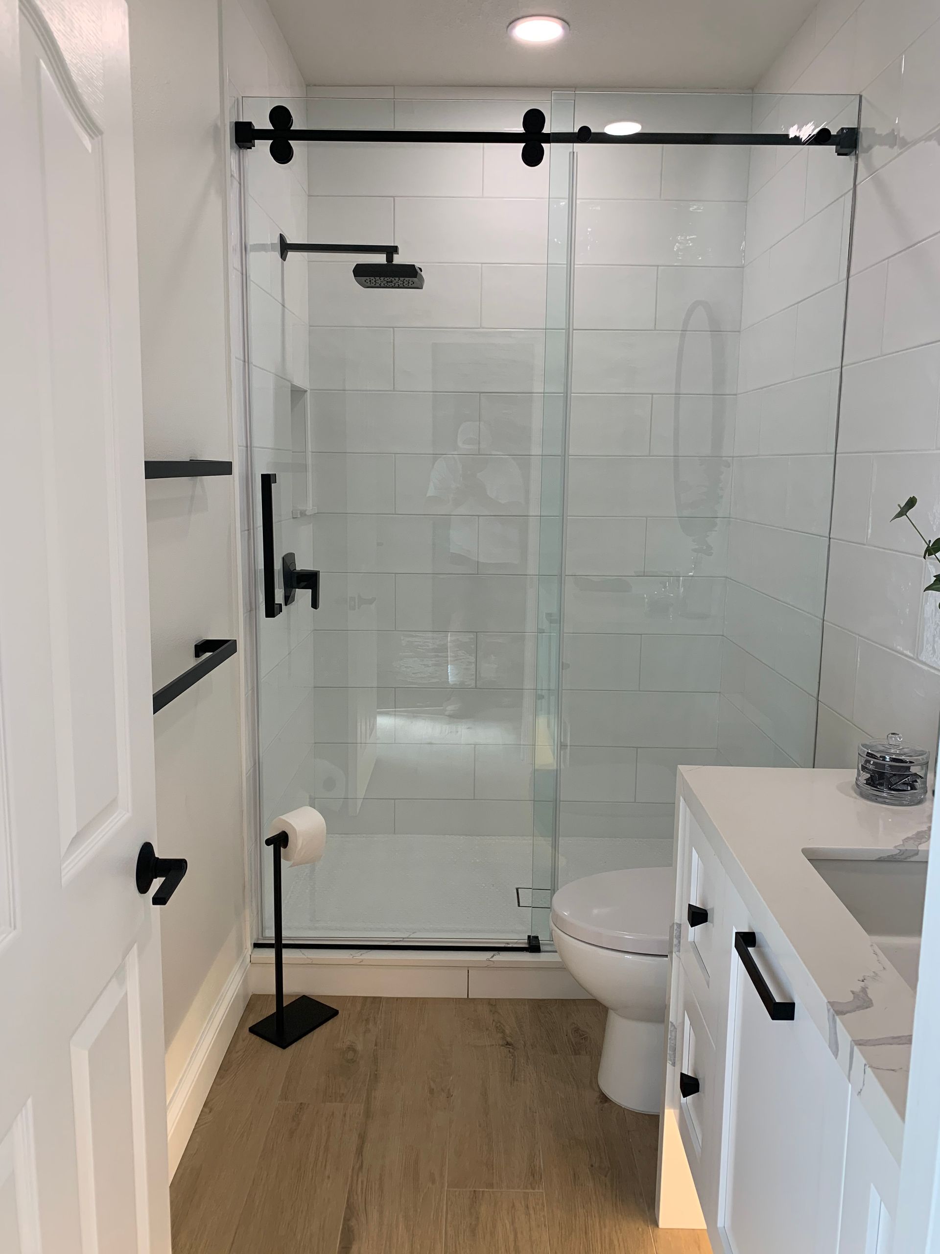 Modern bathroom with glass walk-in shower, white tile, toilet, and wood-look floor