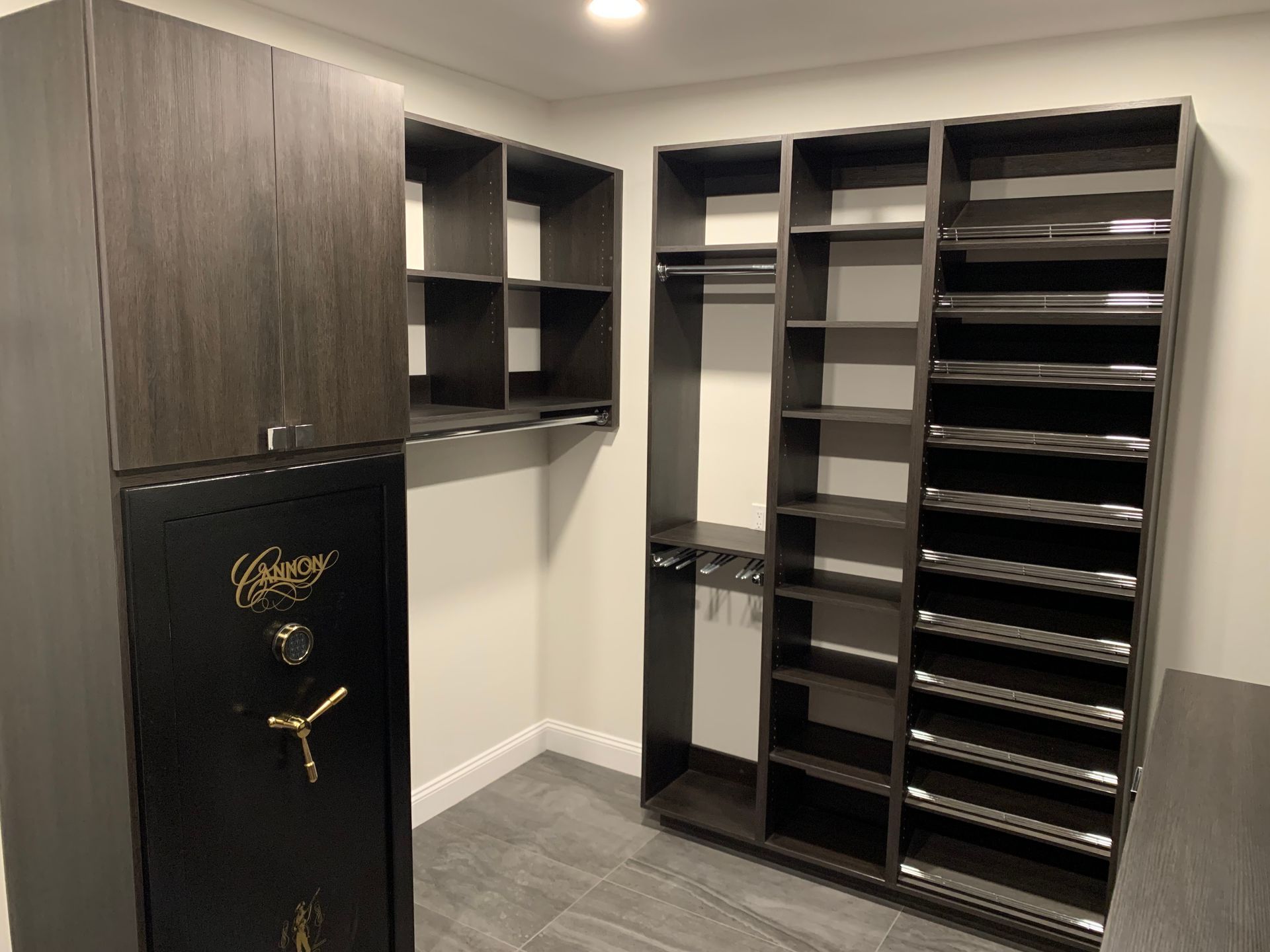 Walk-in closet with dark wood cabinets, open shelving, and a black safe on the left.