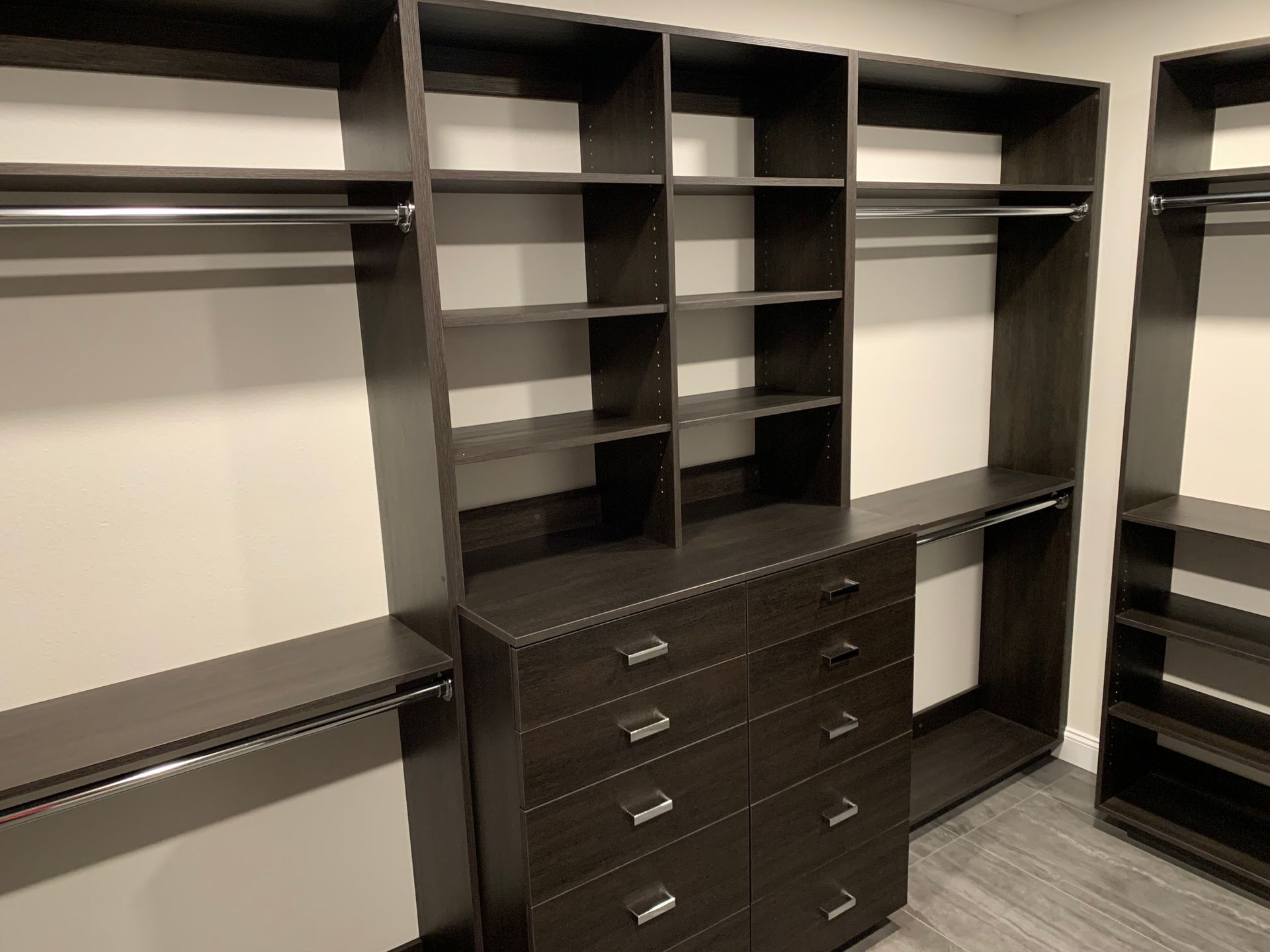 Built-in dark wood closet with open shelves, hanging rods, and drawers in a walk-in dressing room
