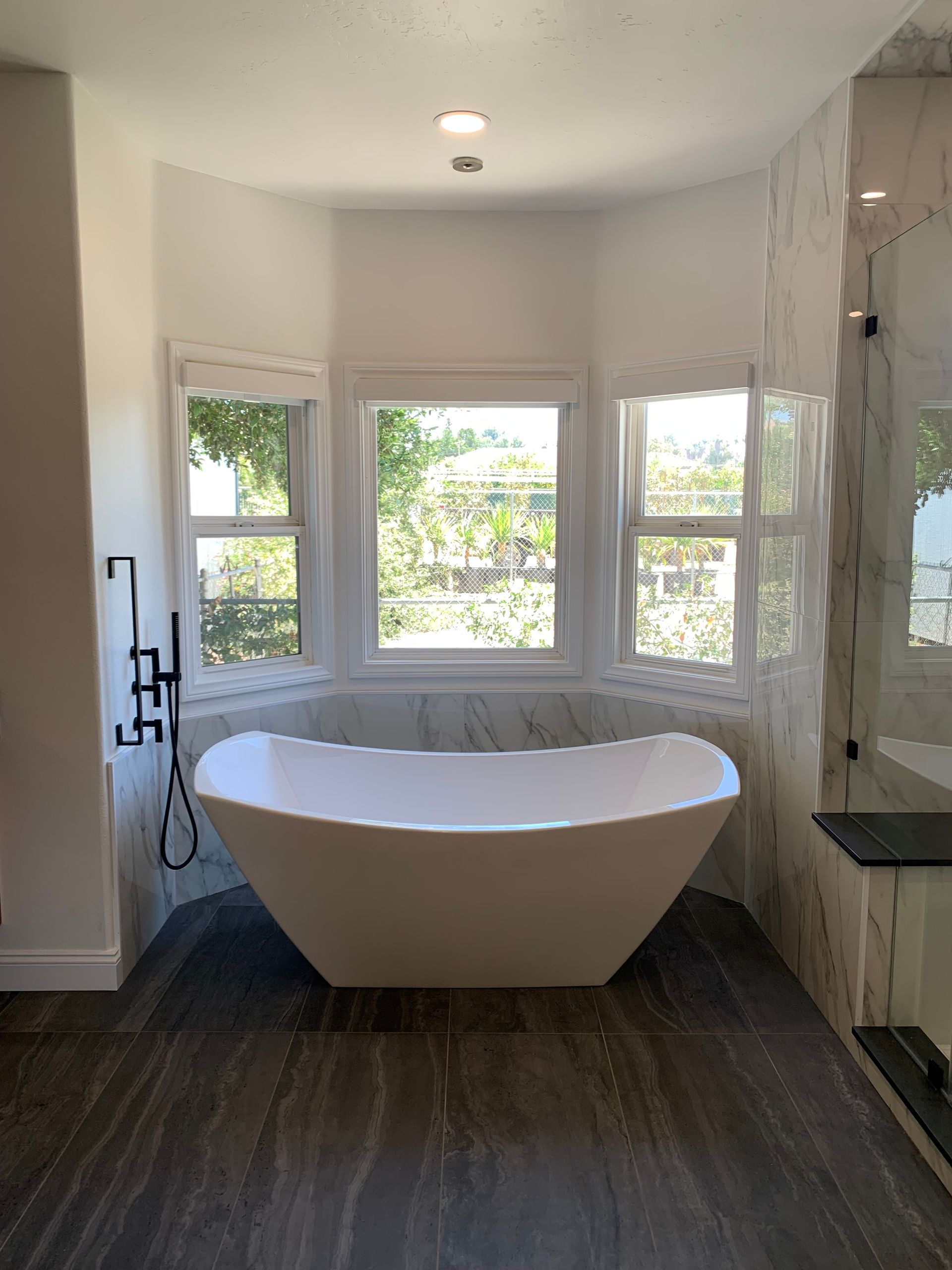 Modern bathroom with a freestanding tub in front of bright bay windows and a glass shower on the right