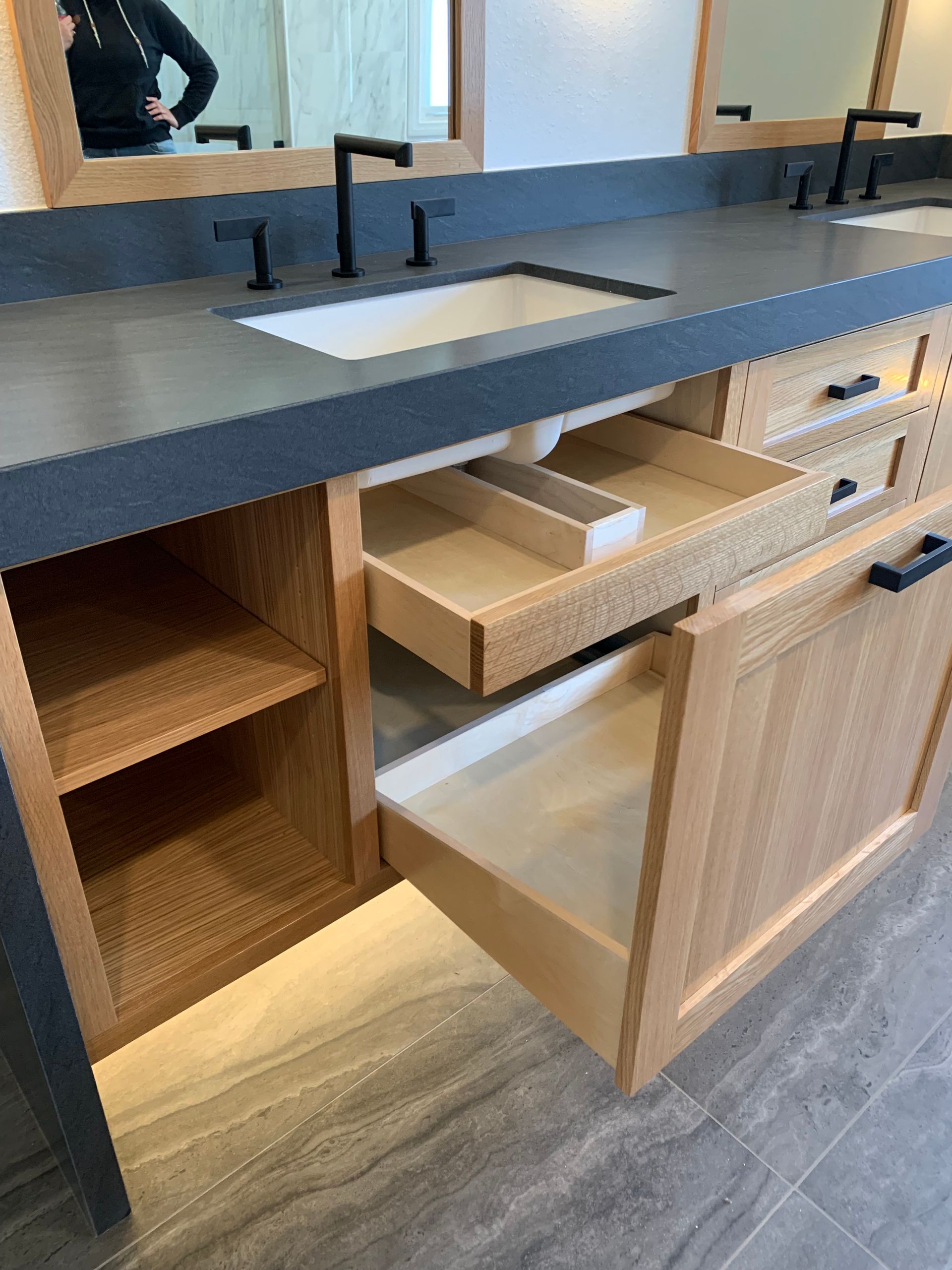 Modern bathroom vanity with black countertop, white sink, wood cabinets, and an open drawer and door