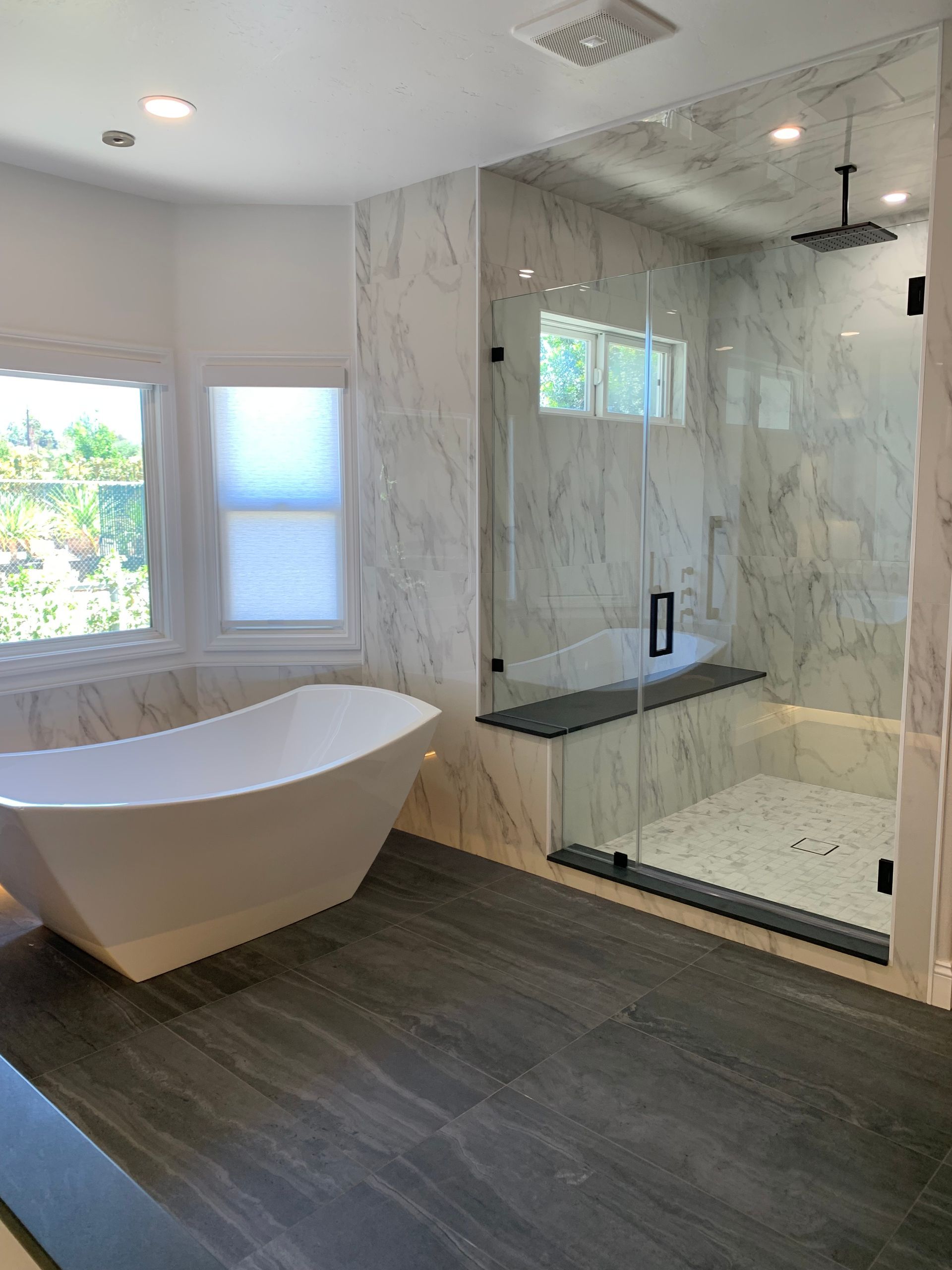 Modern bathroom with freestanding tub, glass shower, marble walls, and dark wood flooring.