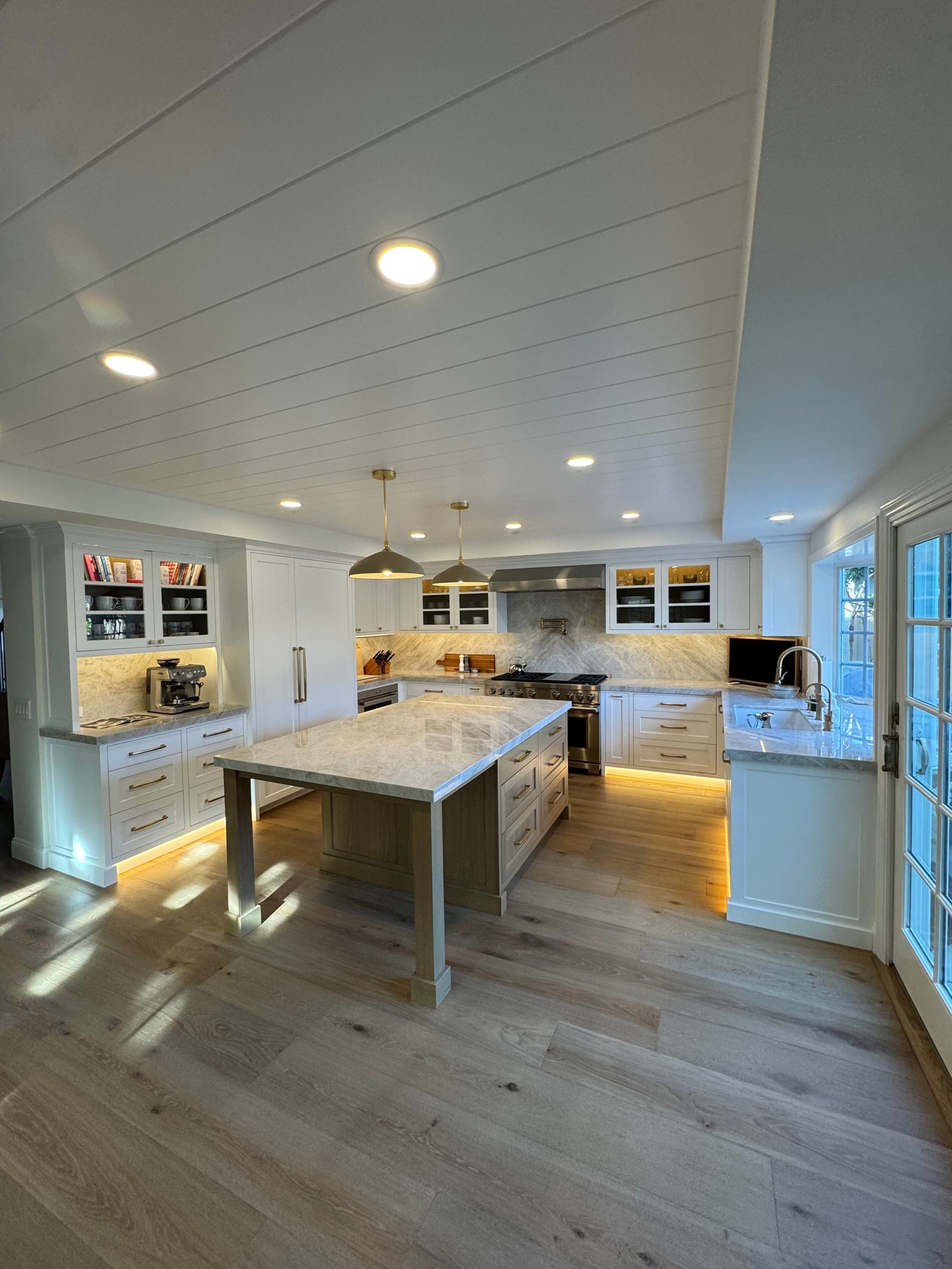 Bright modern kitchen with white cabinets, central island, and hardwood floors with sunlight from windows