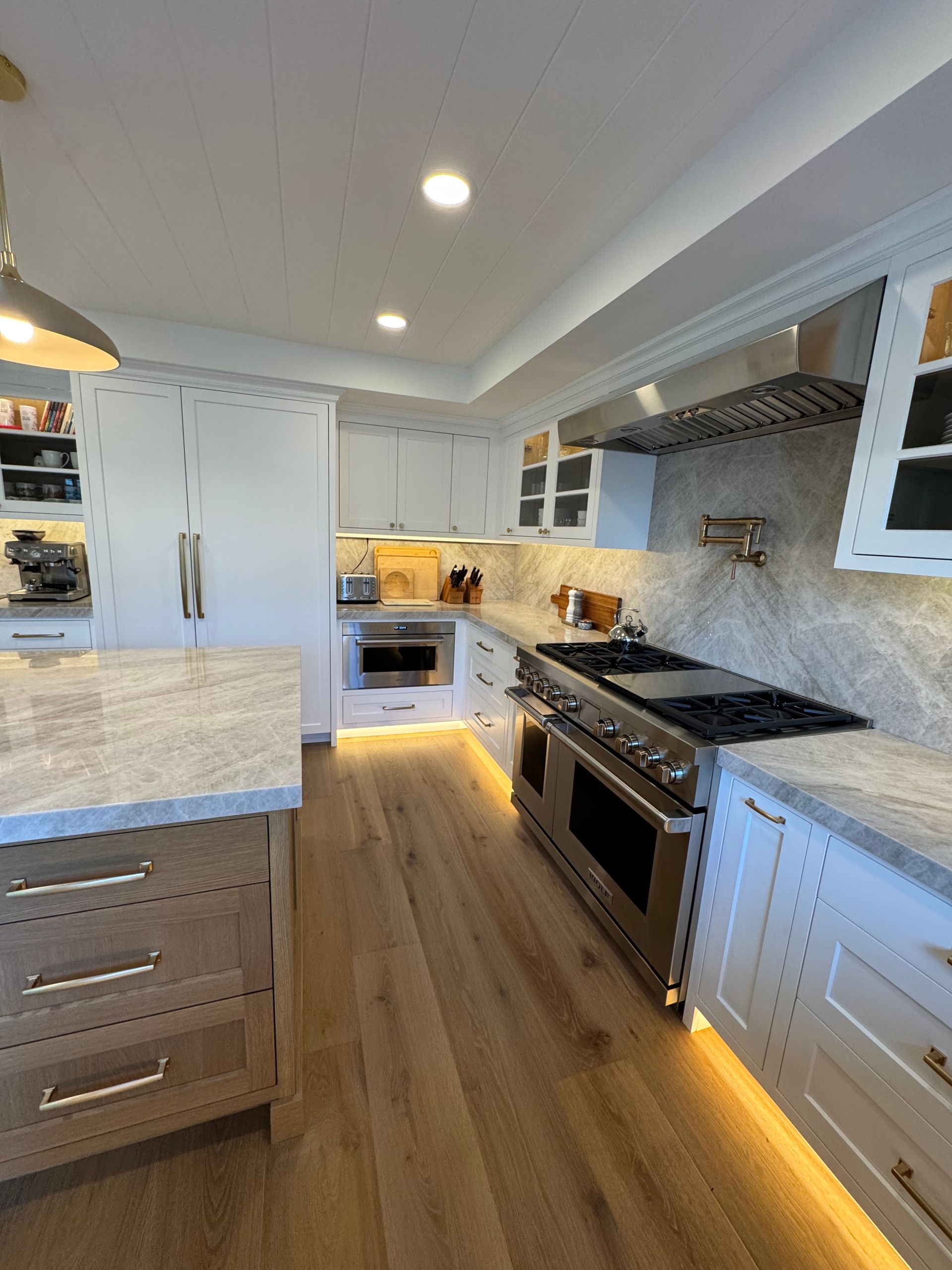 Bright white galley kitchen with stainless appliances, wood floor, and recessed ceiling lights.