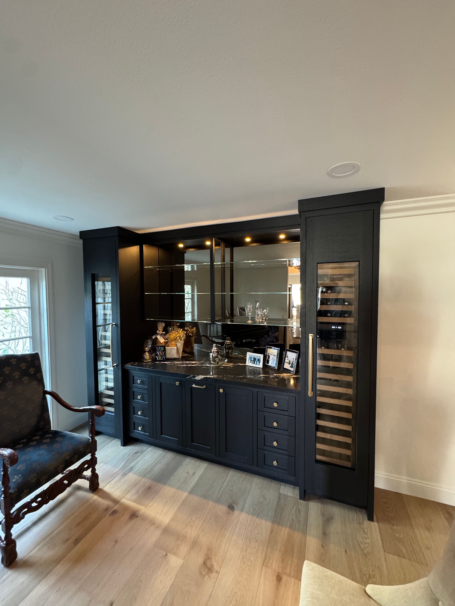 Black built-in bar cabinet with mirrored back, bottles, and glass shelves in a modern living room
