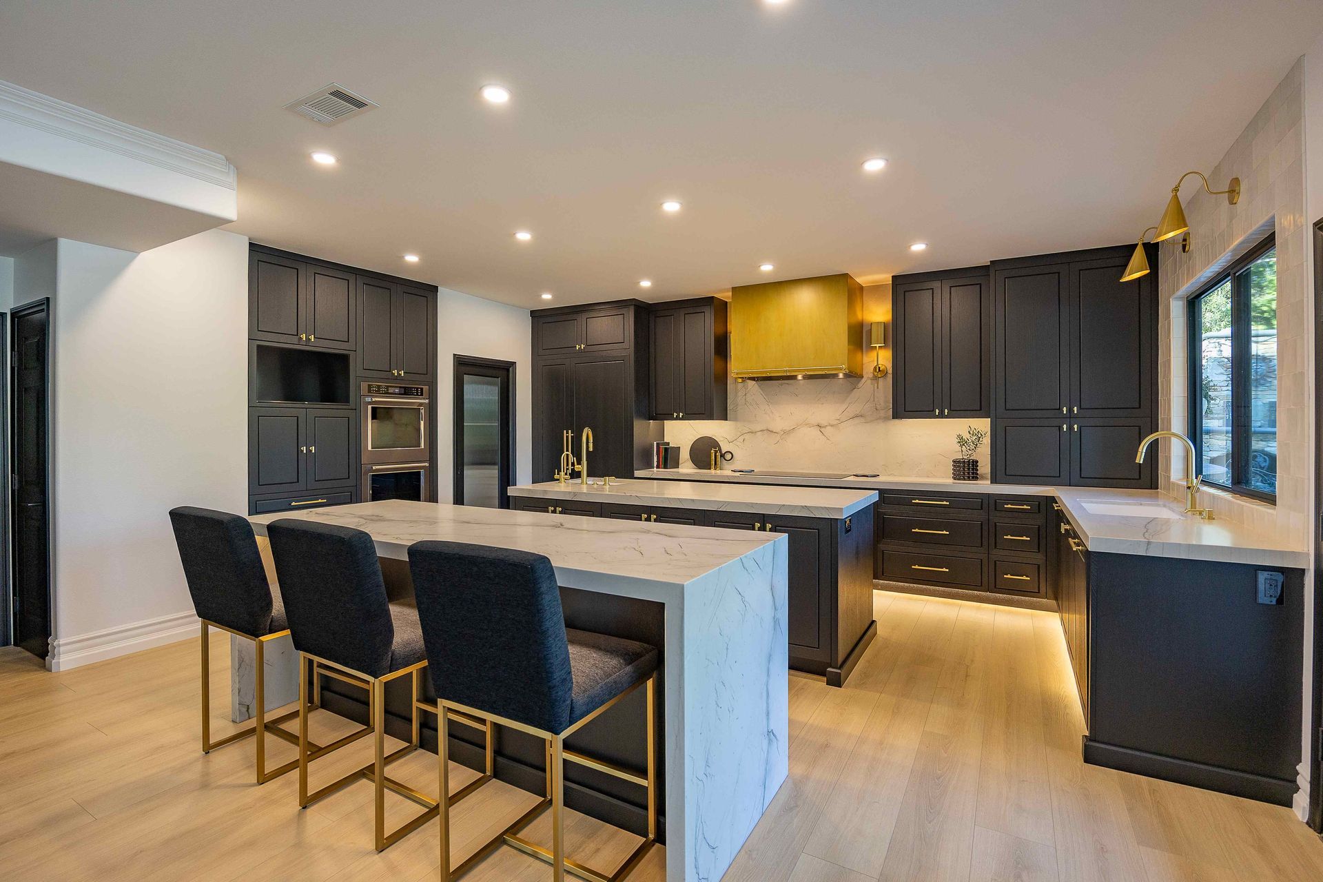 Modern kitchen with dark cabinets, large island, bar stools, and light wood floors