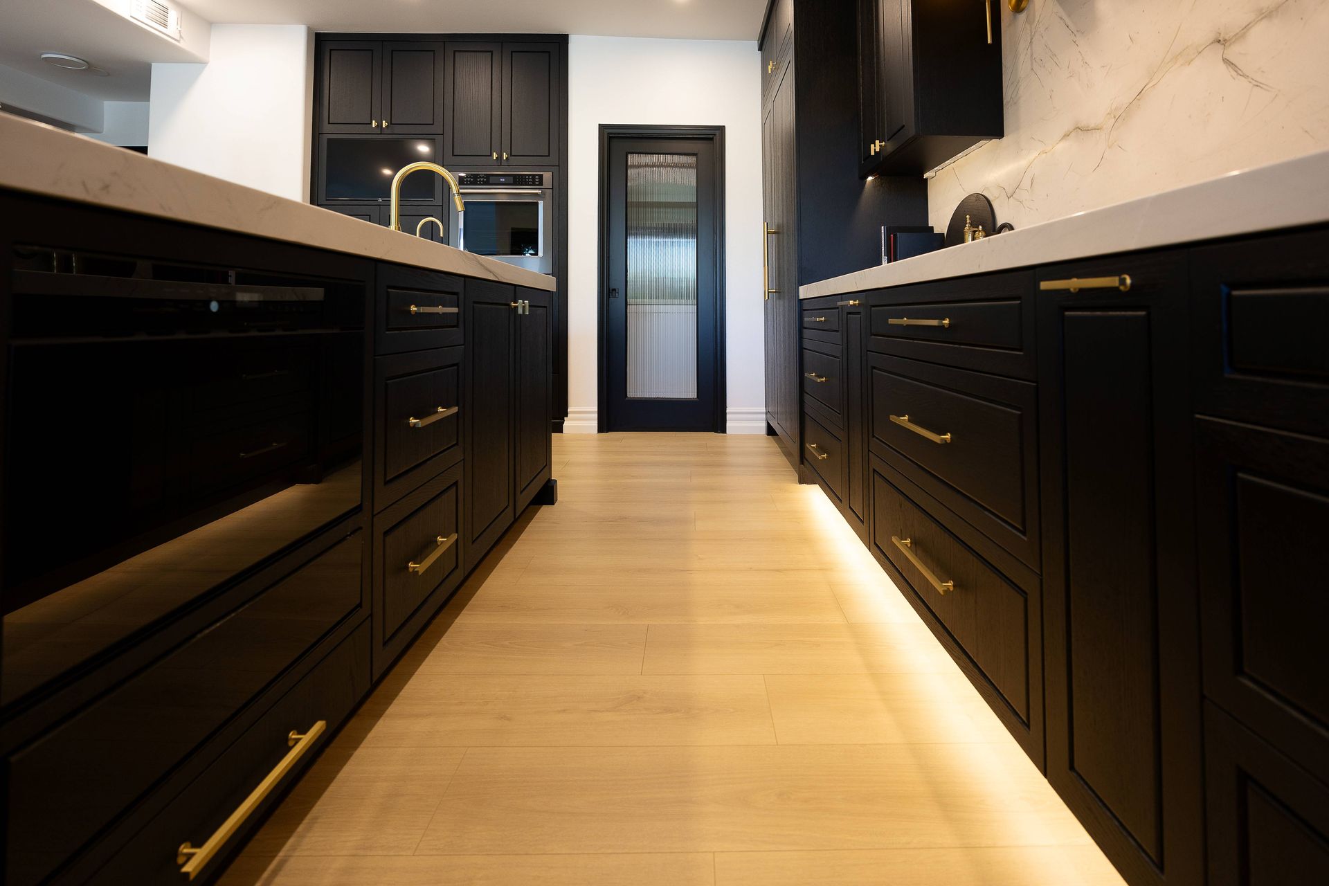 Modern galley kitchen with black cabinets, light wood floor, and white marble countertops