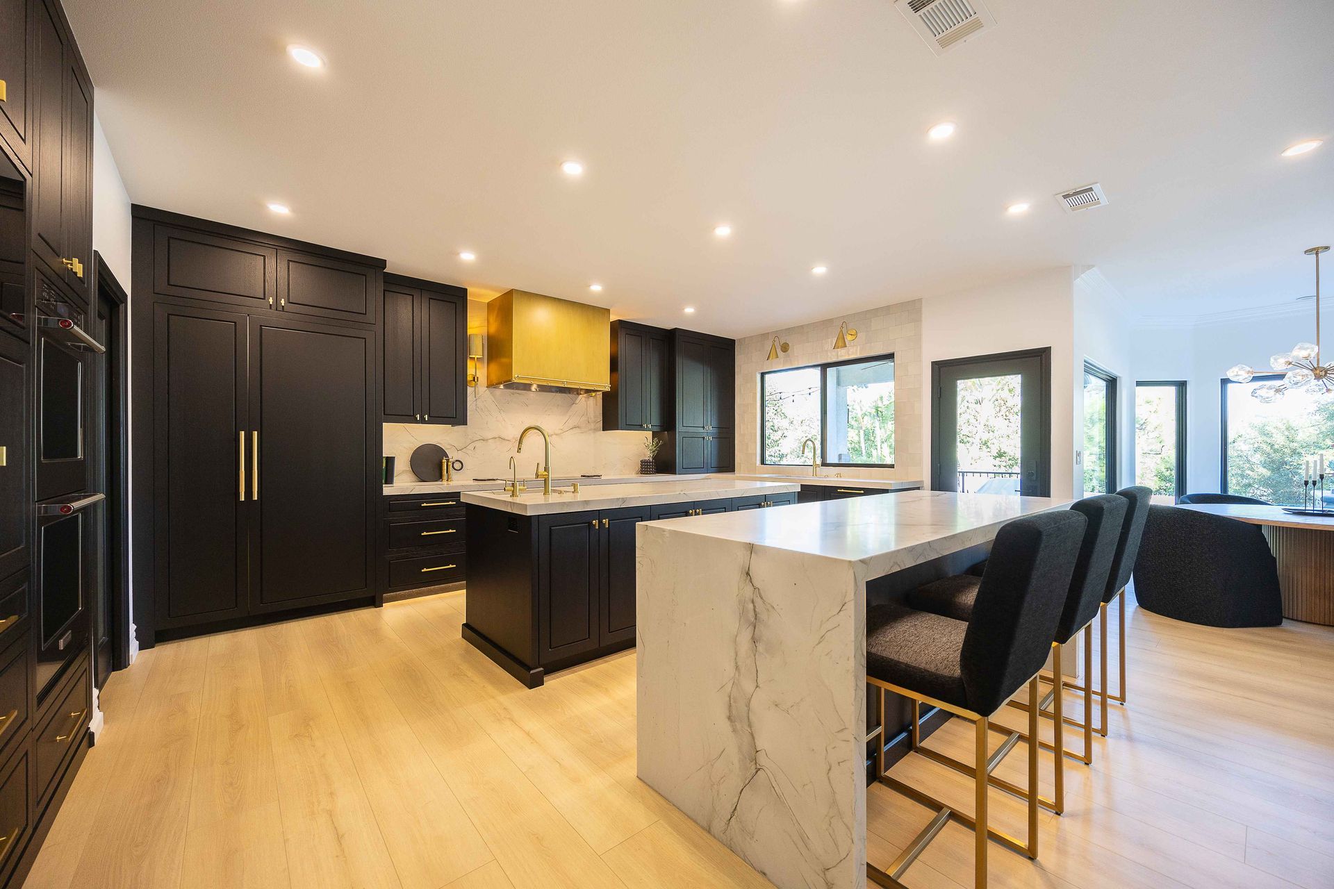 Modern kitchen with black cabinets, marble island, and bar stools in a bright open-concept home