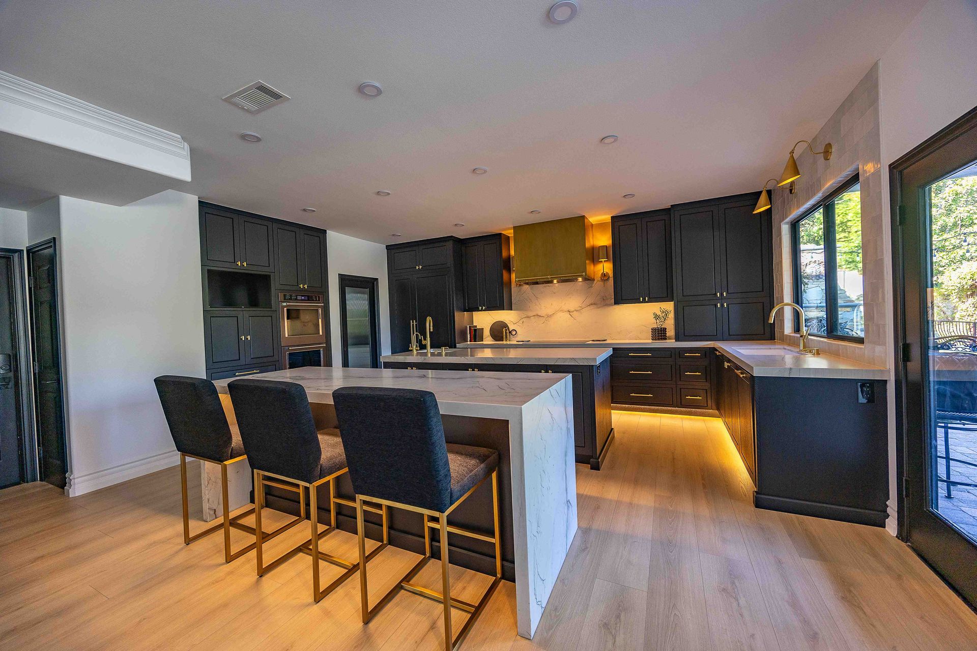 Modern kitchen with dark cabinets, large island, bar stools, and warm under-cabinet lighting