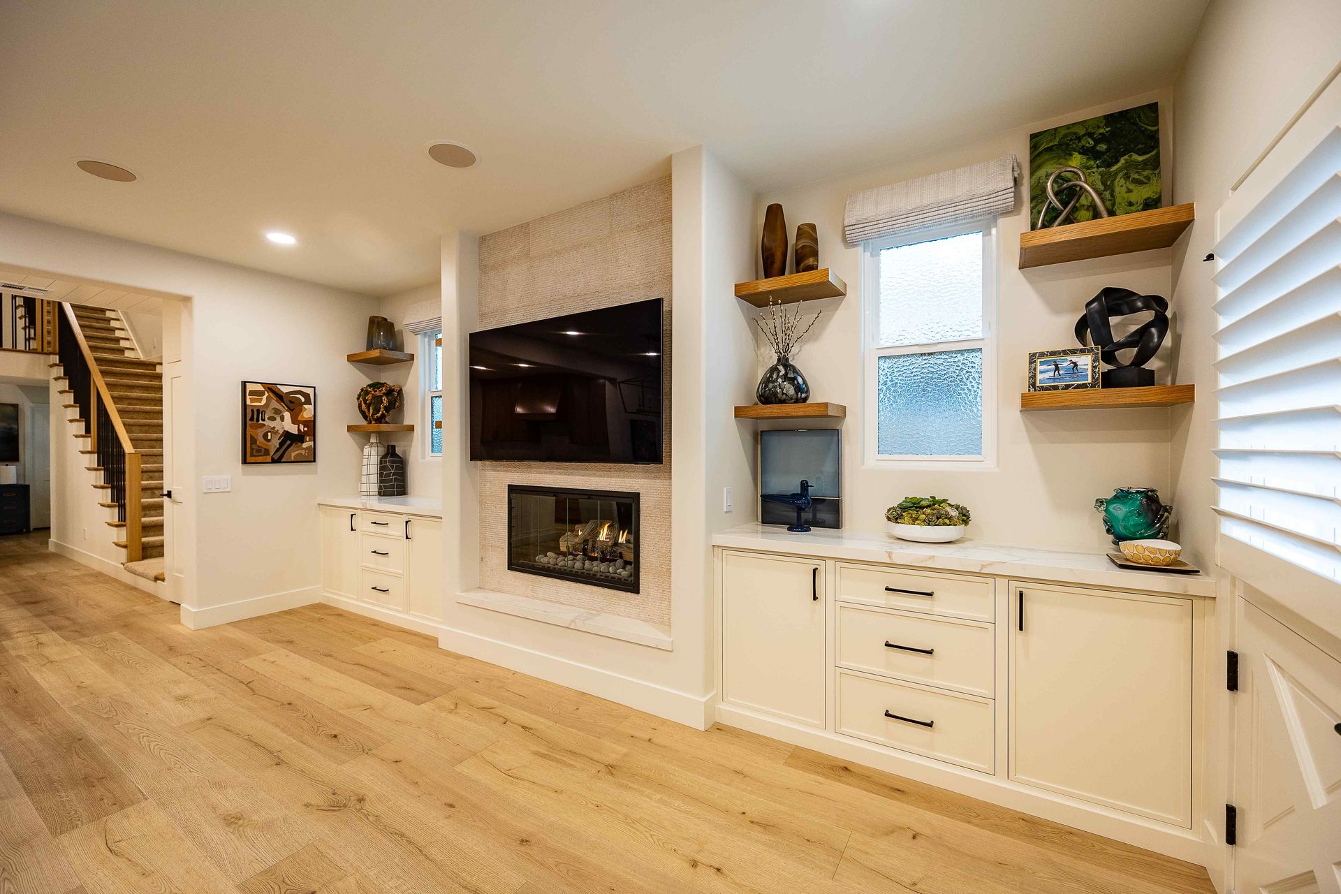 Bright living room with built-in shelves, fireplace, wall-mounted TV, and staircase on hardwood floors