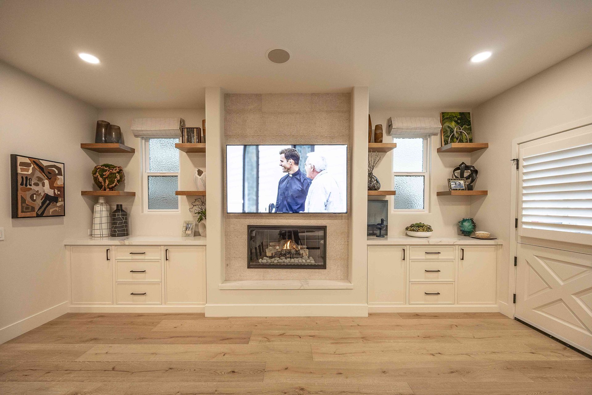Bright living room with built-in shelves, fireplace, TV, white cabinetry, and wood floors