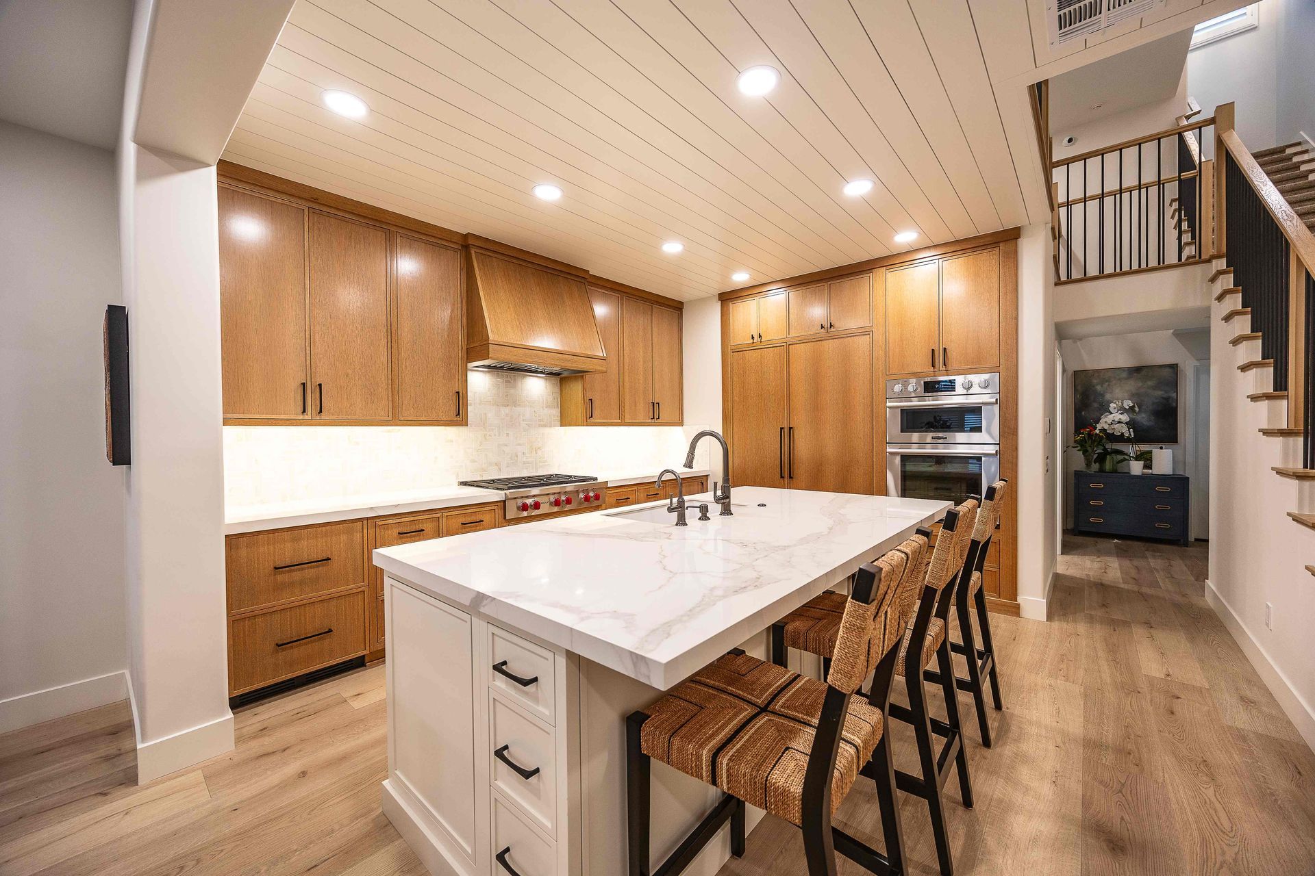 Bright modern kitchen with white island, wood cabinets, and bar stools, seen from an open living space