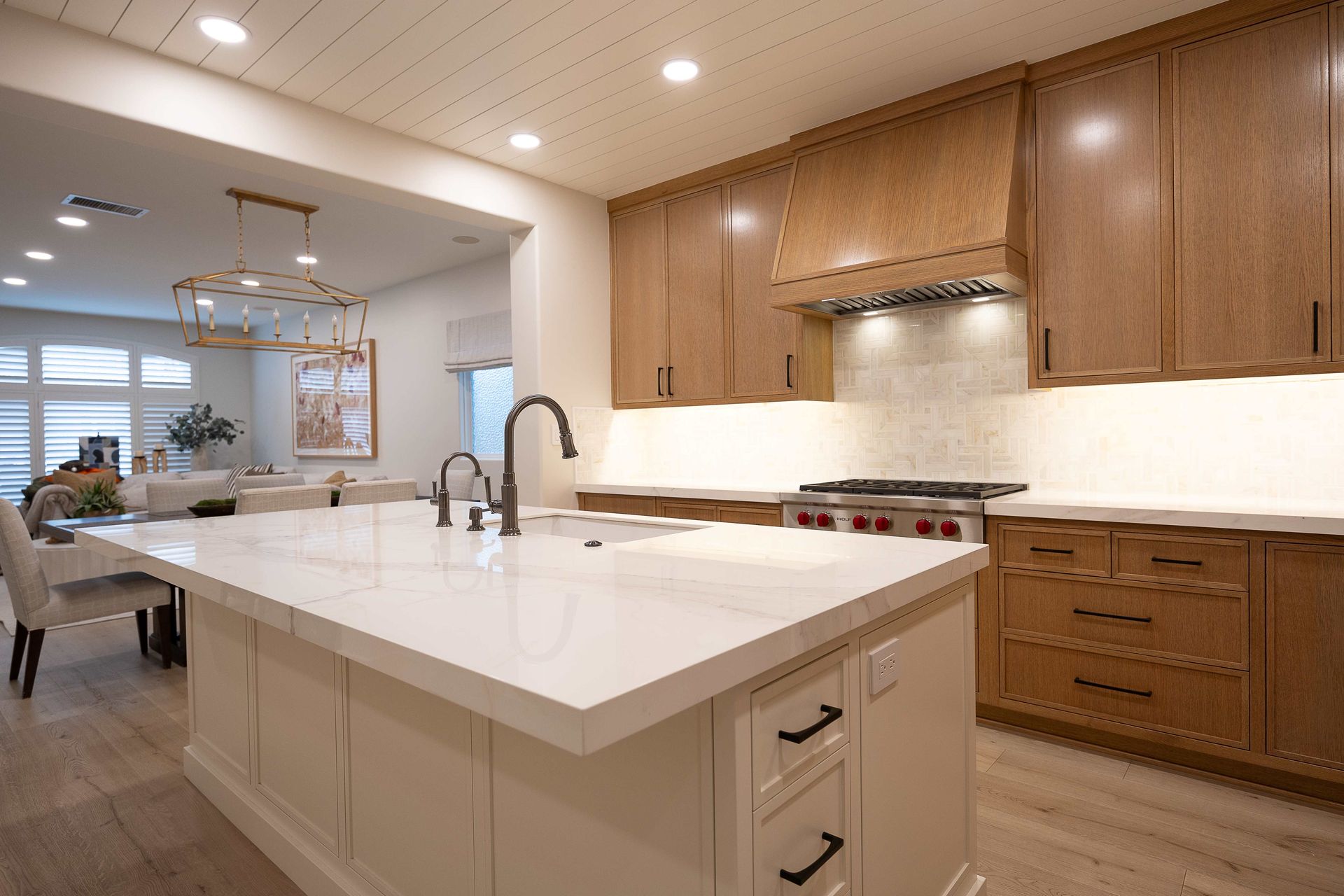 Modern kitchen with white island, wood cabinets, stainless hood, and bright open dining area