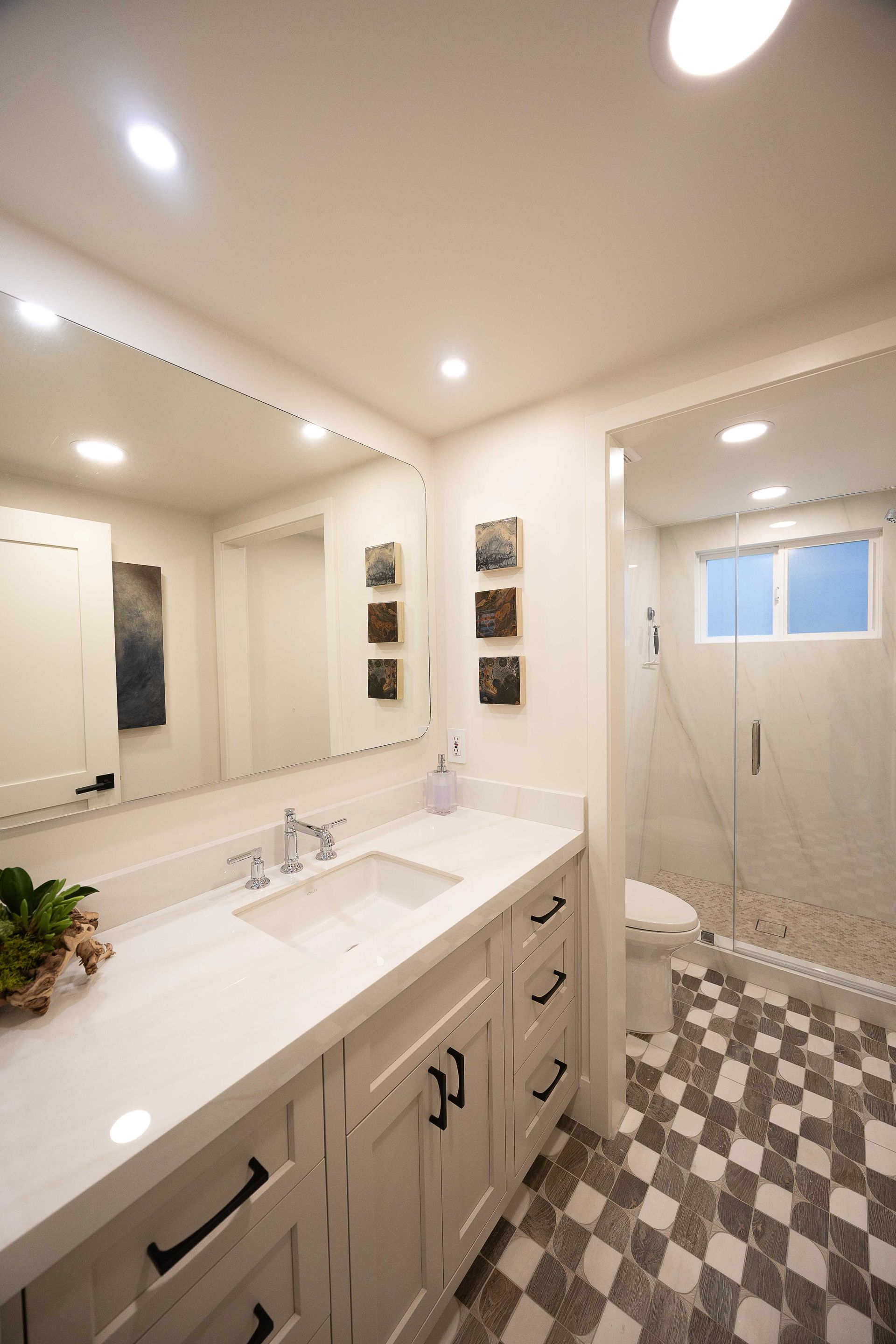 Bright modern bathroom with double vanity, large mirror, walk-in shower, and patterned floor tiles.