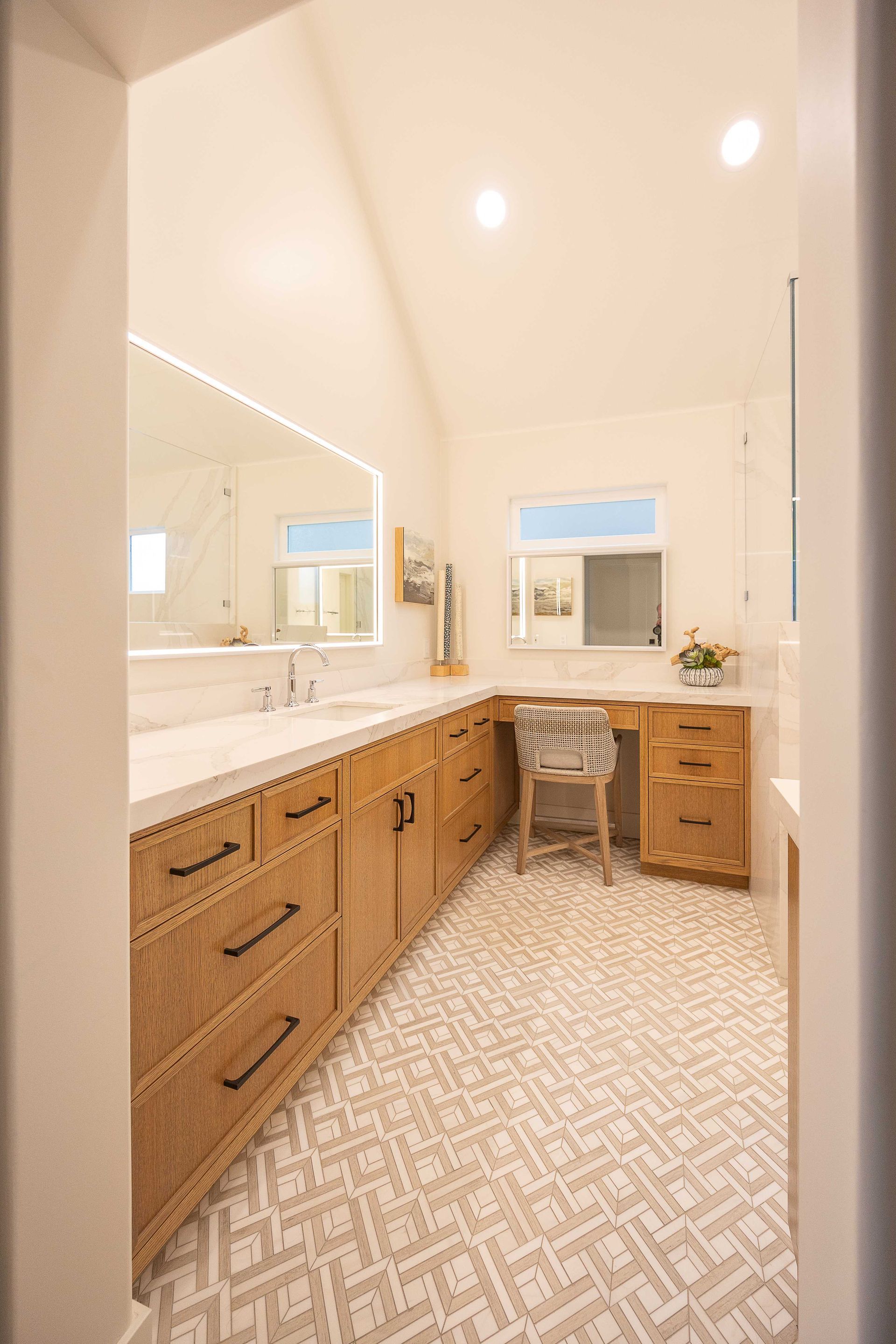 Bright bathroom with double vanity, wicker cabinets, patterned floor, and a small desk by the window.