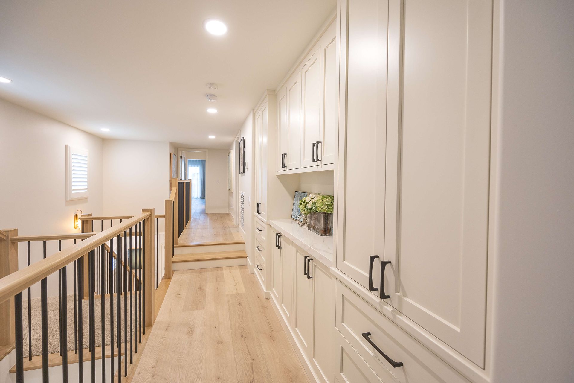 Bright upstairs hallway with light wood floors, white built-in cabinets, and railing overlooking a lower level