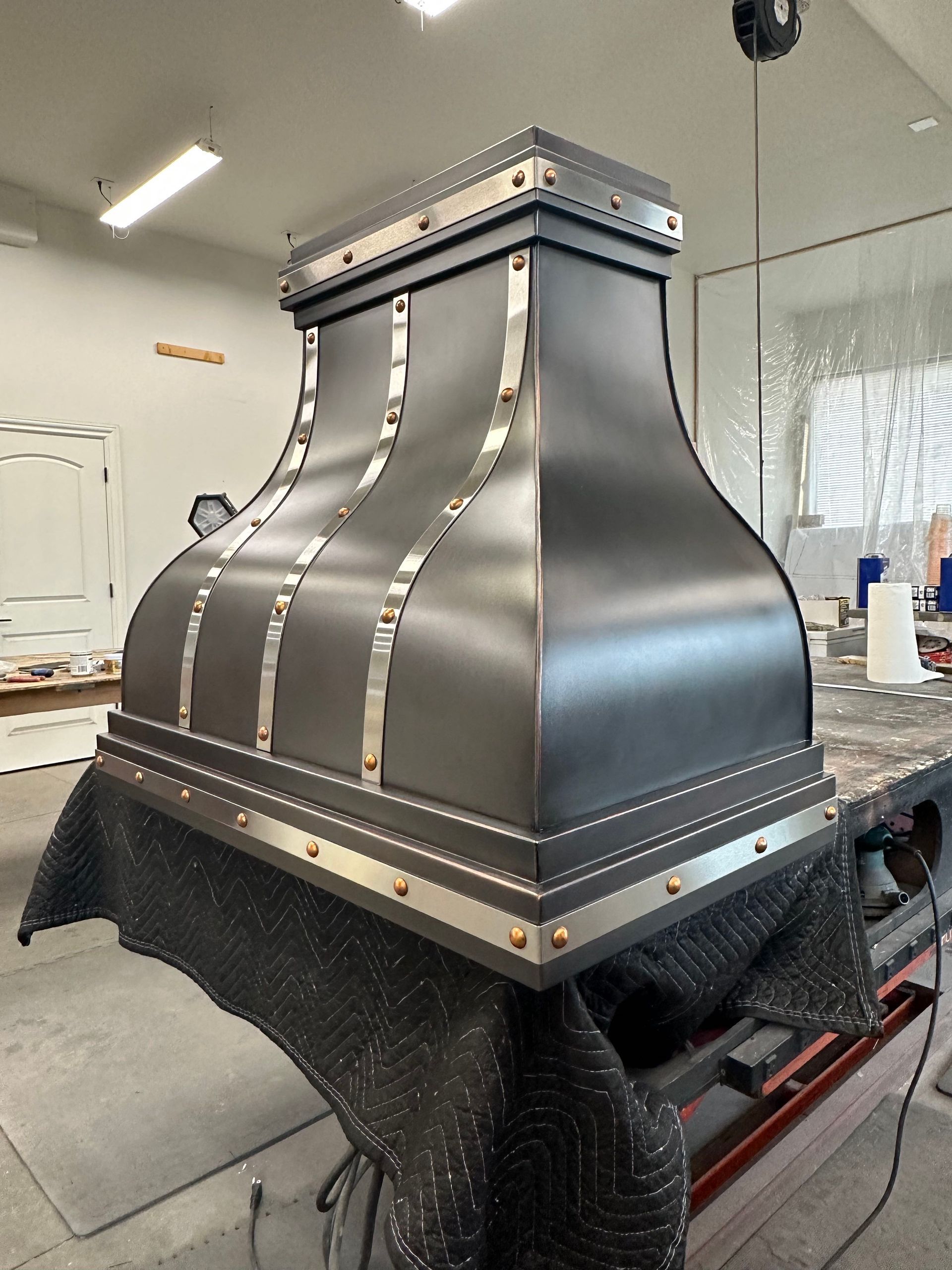 Metal rooftop ventilation hood with dark panels in a workshop, mounted on a black base.
