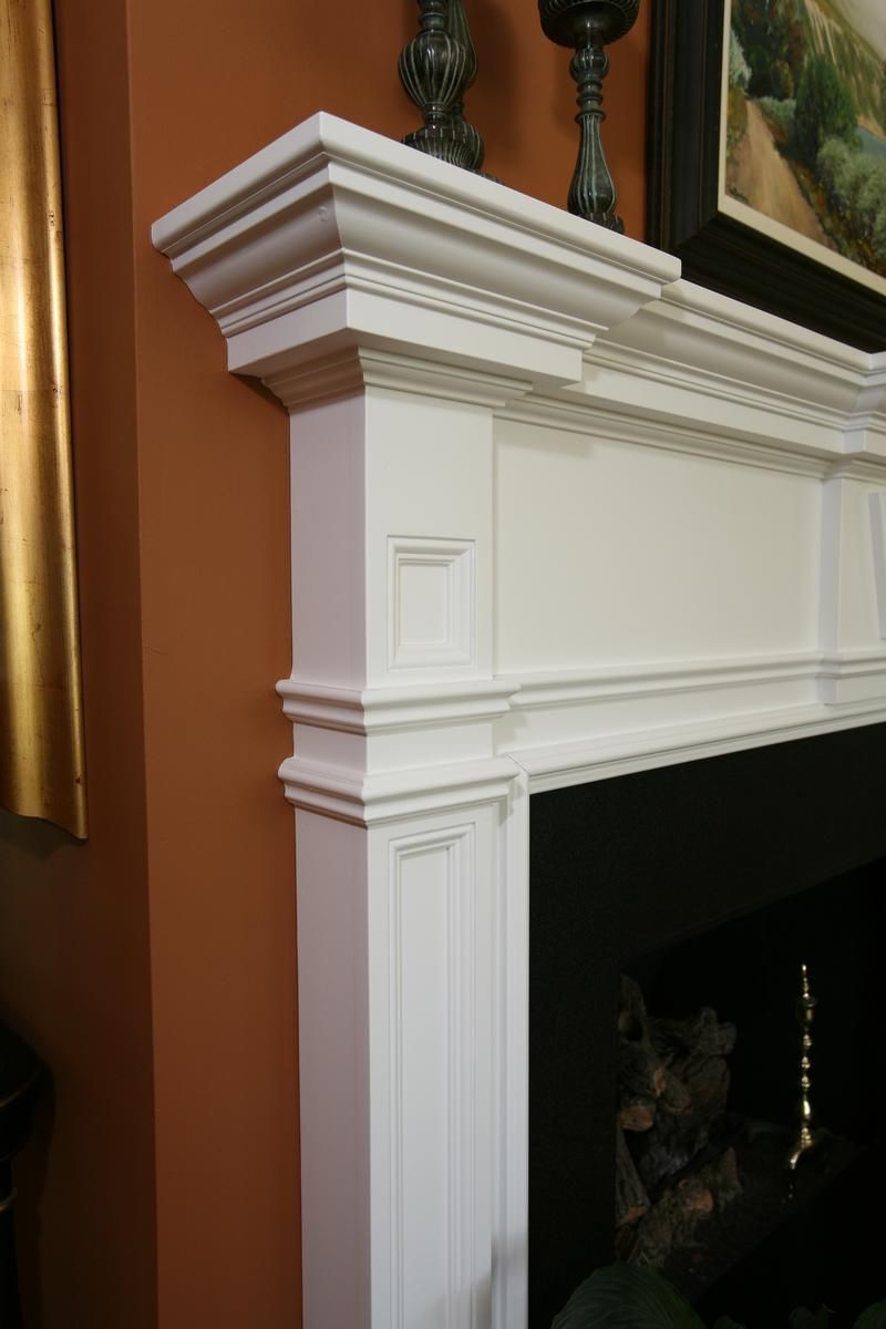 White decorative fireplace mantel with detailed molding against an orange wall, topped with framed artwork and decor
