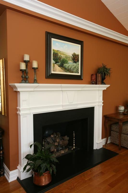 Cozy living room with orange walls, white fireplace mantel, and framed landscape painting above it