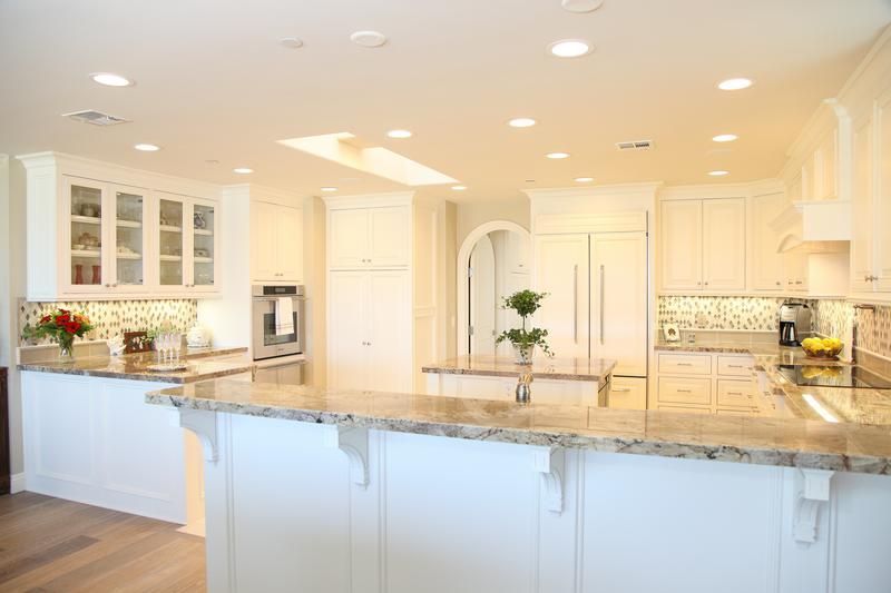 Bright modern kitchen with white cabinets, marble island, and warm recessed lighting