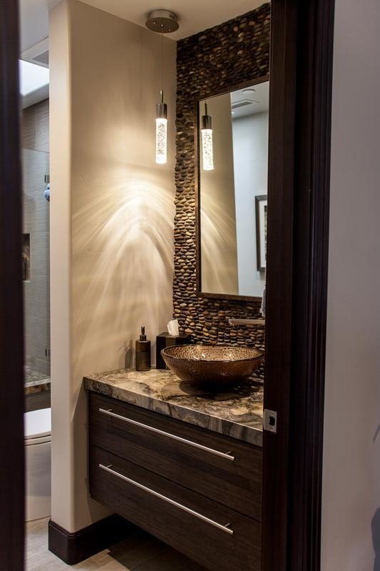Small bathroom vanity with dark wood cabinet, stone sink, and decorative mirror against beige walls