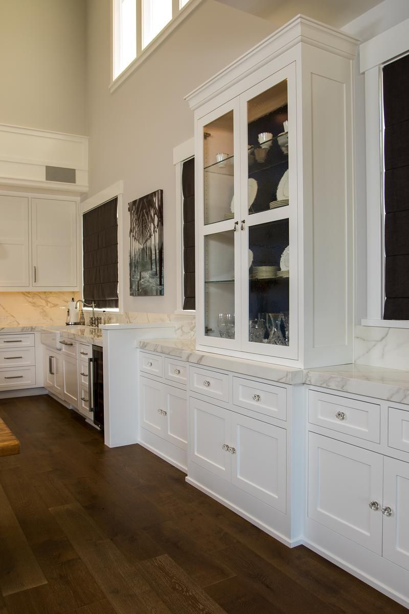 White built-in cabinets and glass display hutch in a bright kitchen with dark hardwood floors