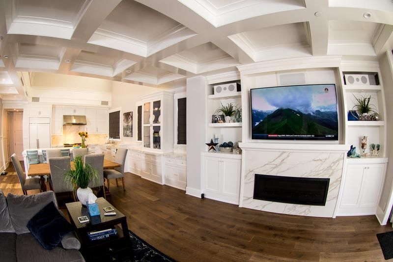 Bright modern living room with white walls, wood floors, fireplace, TV, and black leather seating