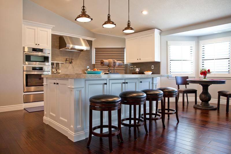 Bright modern kitchen with white cabinets, island, pendant lights, and dark wood floors