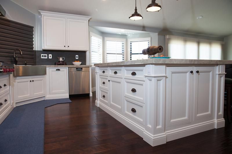 Bright white kitchen with large island, dark wood floors, stainless dishwasher, and windows along the back wall