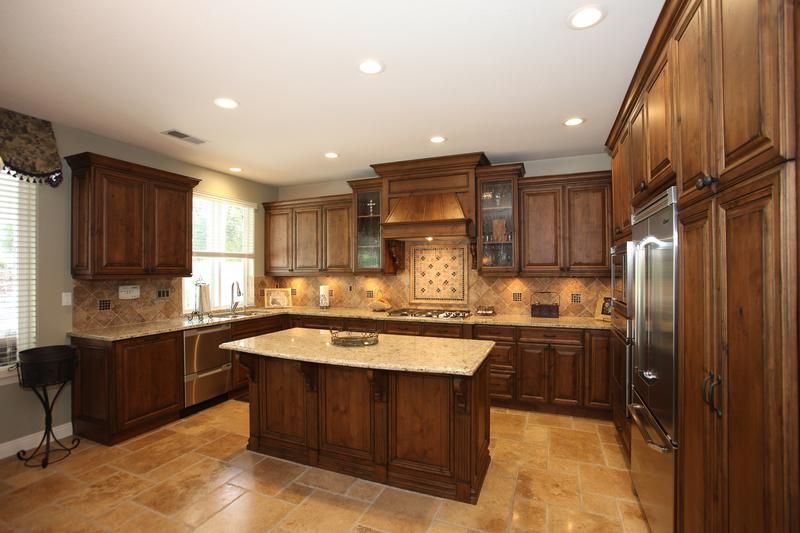 Spacious kitchen with dark wood cabinets, granite island, tiled backsplash, and recessed ceiling lights.
