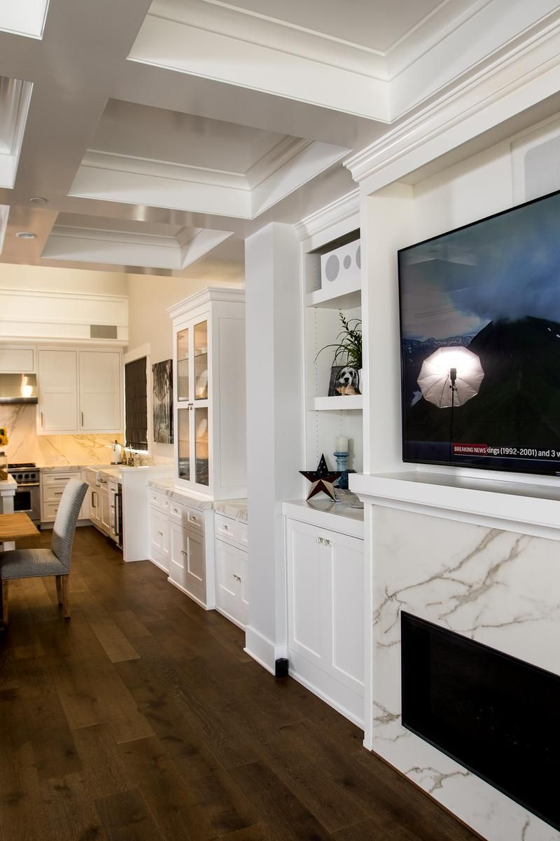 Bright living room with built-in white cabinets, dark wood floors, and a fireplace with a wall-mounted TV.
