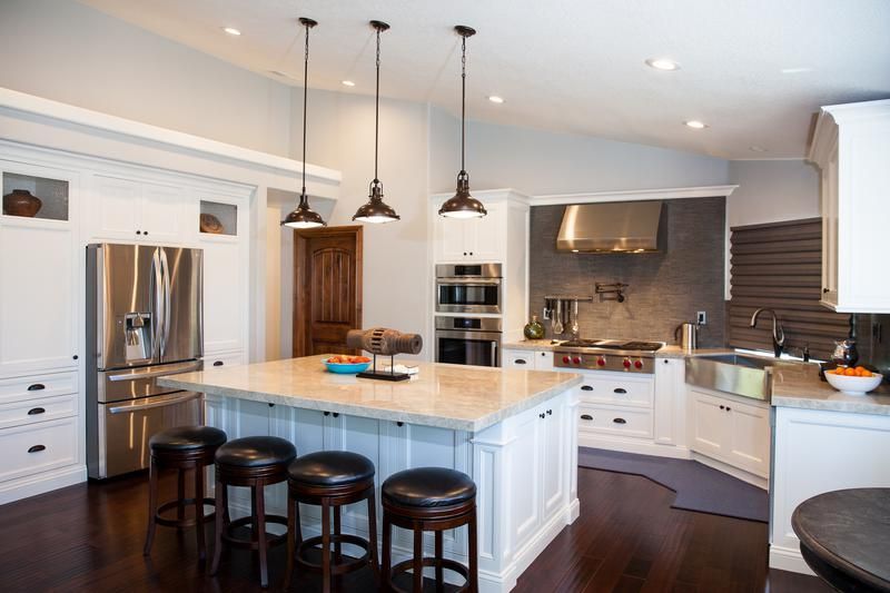 Modern white kitchen with island, dark wood floors, stainless steel appliances, and three bar stools