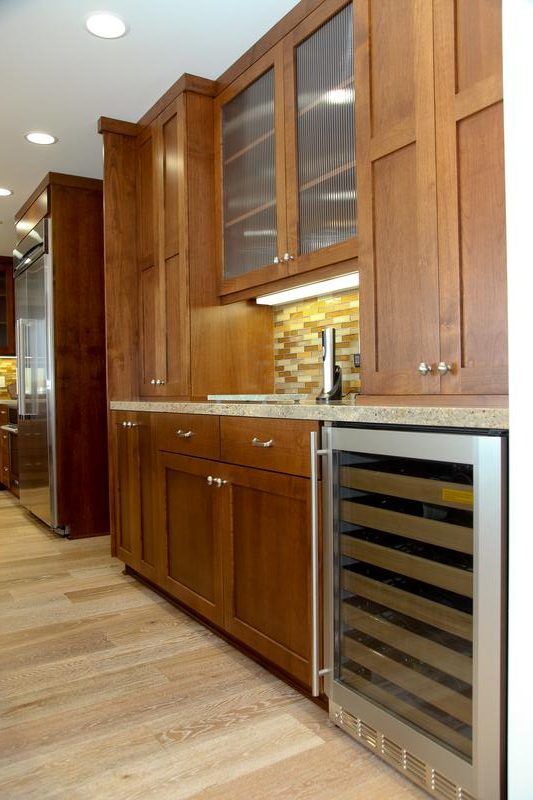 Warm wood kitchen cabinetry with built-in wine cooler and hardwood floor in a modern interior