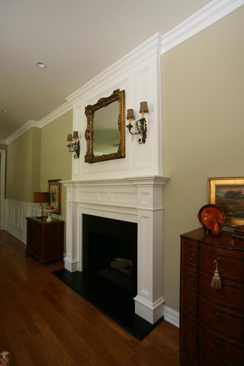 Elegant hallway with white fireplace, mirror, sconces, and wooden floor and furniture