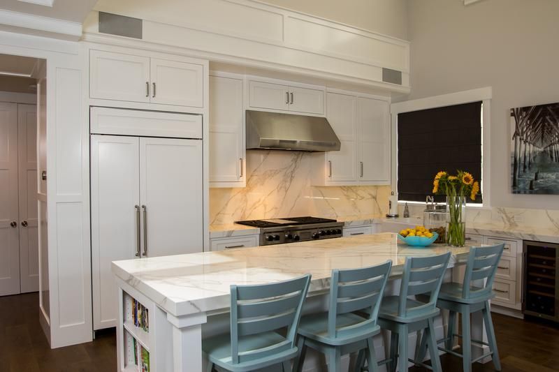 Modern kitchen with white cabinets, marble island, teal stools, and stainless steel appliances