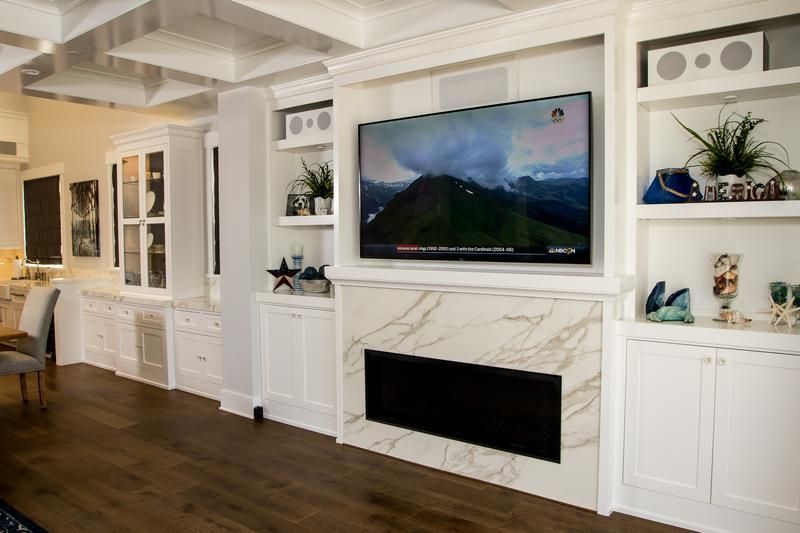 Modern living room with a wall-mounted TV above a white marble fireplace and built-in cabinets on each side
