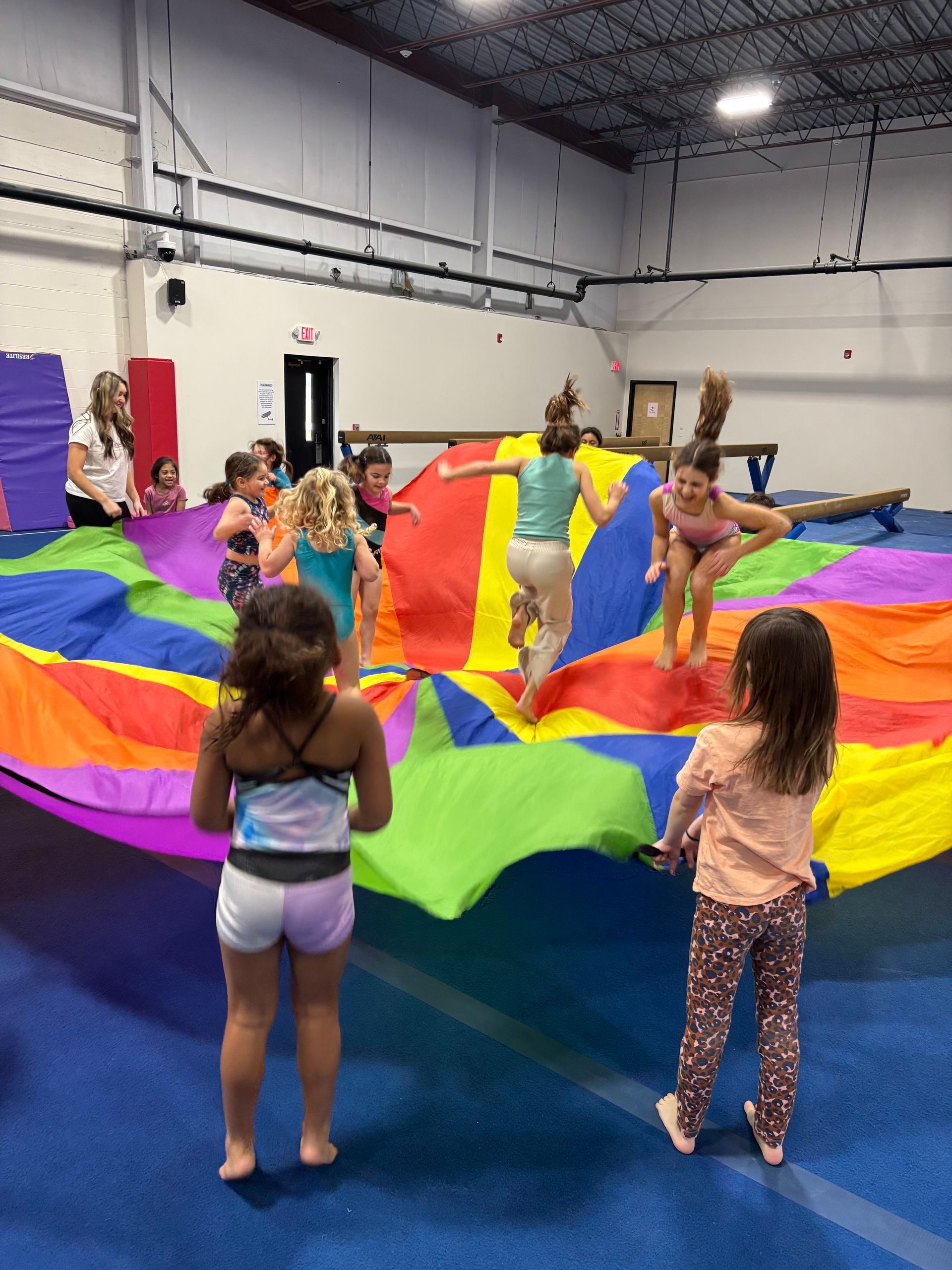 Children playing with a colorful parachute in a gymnasium.