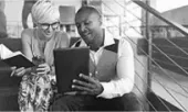 A man and a woman are sitting on a couch looking at a tablet.