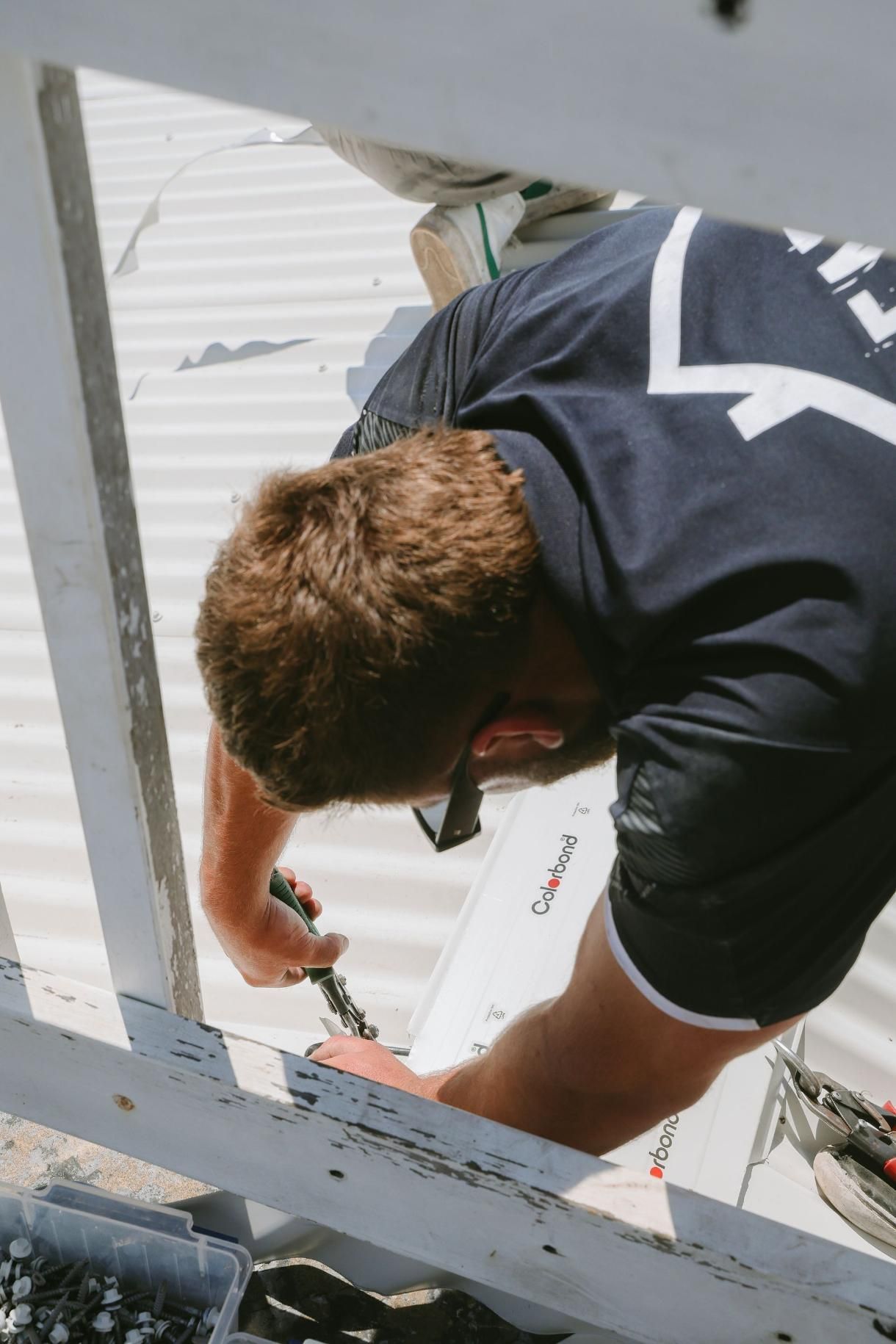 Man is Working on a Roof With a Screwdriver — Beards Roofing and Plumbing in Clontarf, QLD