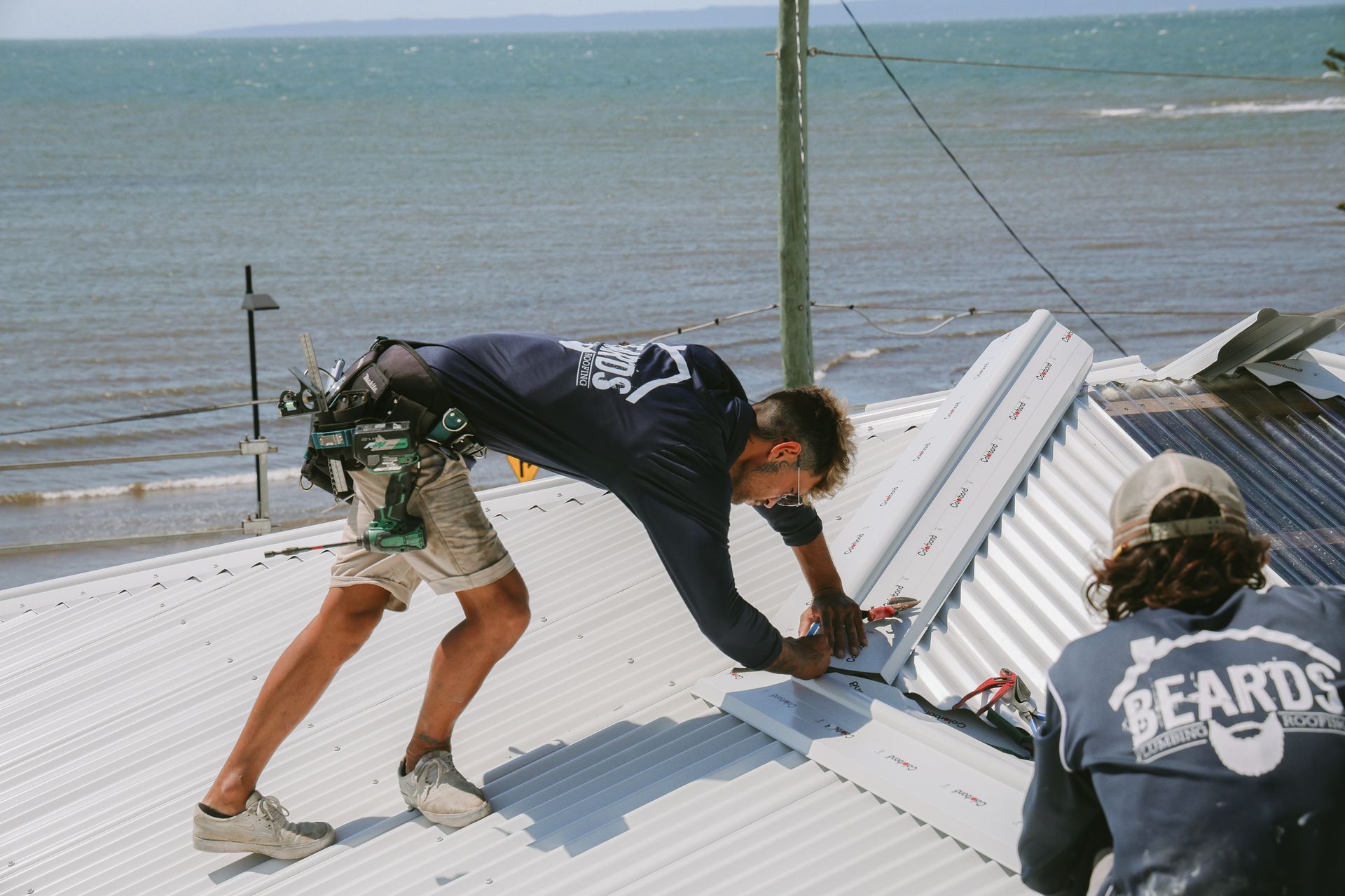 Two men are working on a roof with one wearing a shirt that says beard