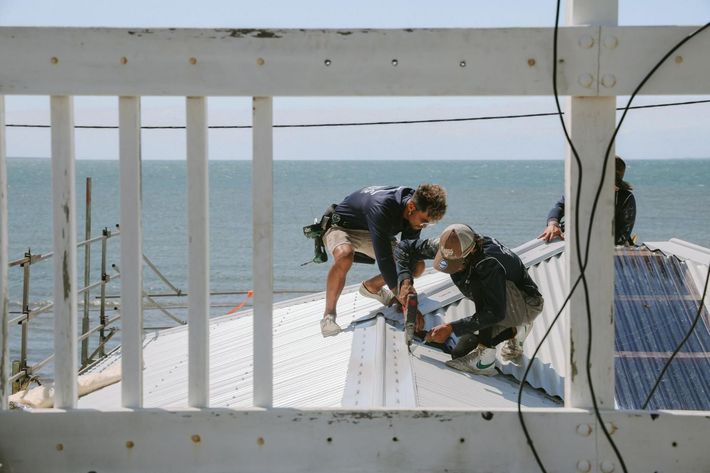 Two Men Working On A Roof With The Ocean In The Background — Beards Roofing and Plumbing in Clontarf, QLD