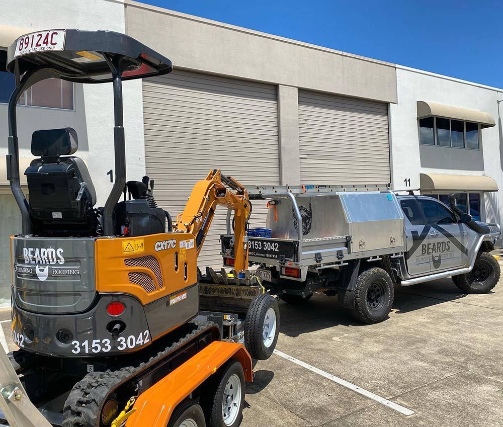 A Small Excavator is Parked Next to a Truck in a Parking Lot — Beards Roofing and Plumbing in Burpengary, QLD