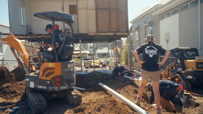 A Man Driving A Bobcat On Dirt And People Working Around Him — Beards Roofing and Plumbing in Clontarf, QLD