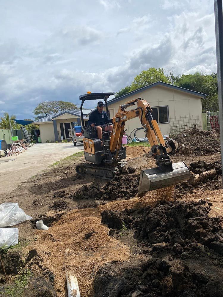 A Man is Driving a Small Excavator on a Dirt Road — Beards Roofing and Plumbing in Kallangur, QLD