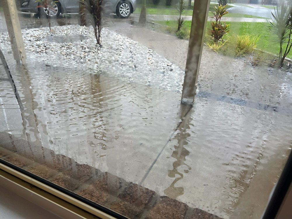 A Window Shows a Flooded Driveway With a Car Parked in the Background — Beards Roofing and Plumbing in Burpengary, QLD