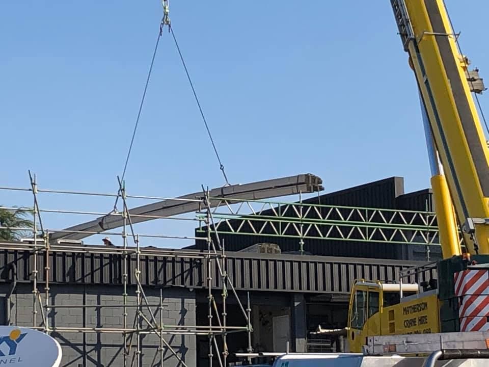 A Large Yellow Crane is Lifting a Large Piece of Metal — Beards Roofing and Plumbing in Ipswich, QLD