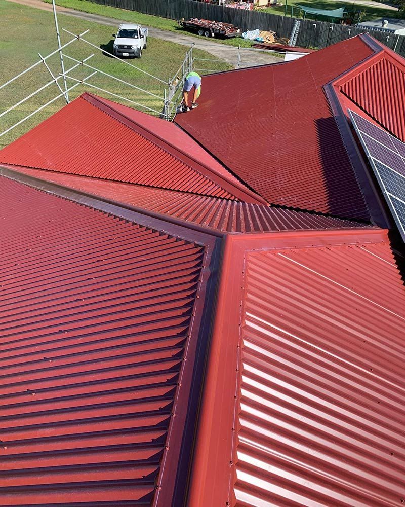 A Man is Standing on Top of a Red Roof — Beards Roofing and Plumbing in Redcliffe, QLD