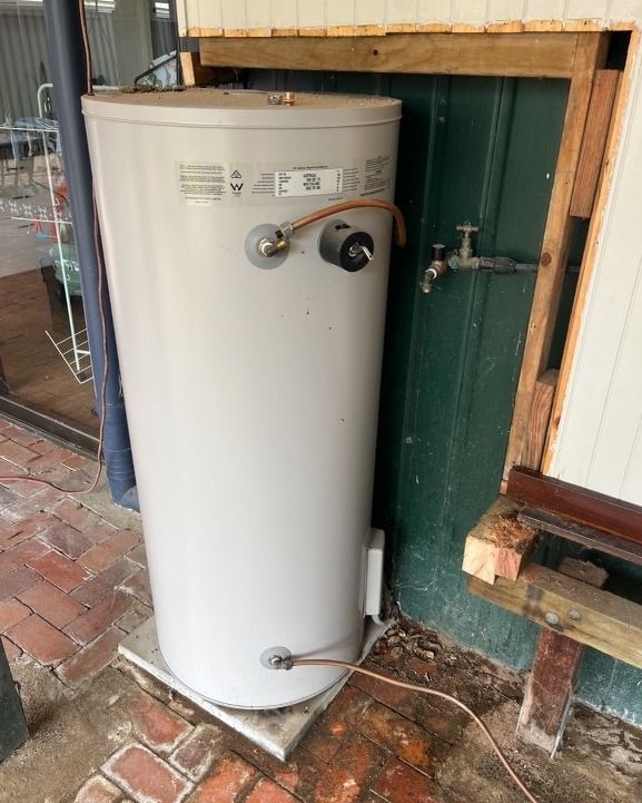 A white water heater is sitting next to a green wall.