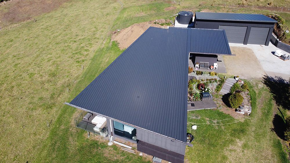 An Aerial View of a House With a Black Roof in a Grassy Field — Beards Roofing and Plumbing in Kallangur, QLD